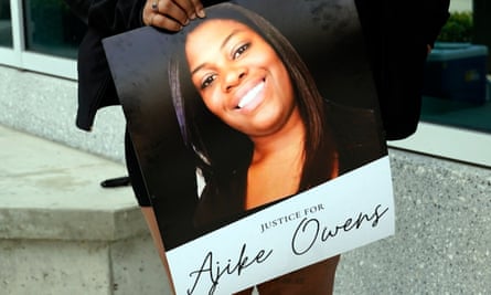 A person holds a poster of a Black woman smiling with the text ‘Justice for Ajike Owens’ underneath