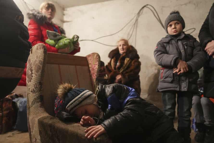 A child sleeps in an armchair as others stand around in a shelter during Russian shelling, in Mariupol.