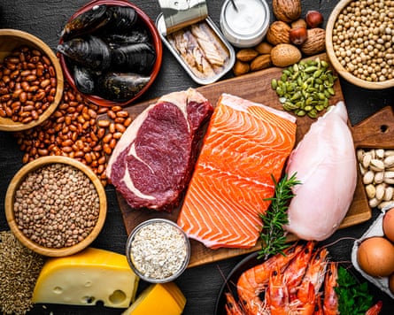 Overhead view of a large group of food with high content of healthy proteins. The composition includes salmon beef fillet, chicken breast, eggs, yogurt, mussels, chick peas, pistachios, cheese, brown lentild, beans, shrimps, canned tuna, pumpkin seeds, soybeans among others.