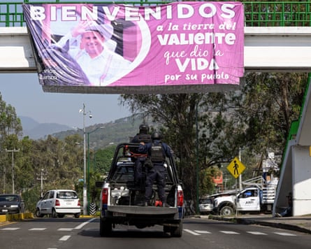 Agents pass under a bridge bearing a banner of Carlos Manzo