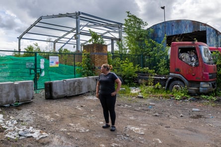 Rowson stands outside metal fencing which has green canvas hung on it, while alongside is a rusting red truck and corrugated barn