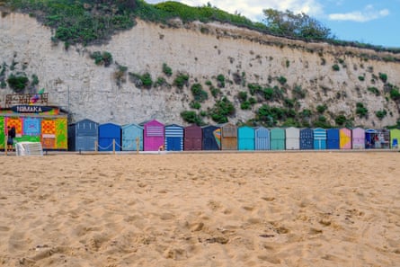 Picturesque sandy beach with row of vibrant, colourful beach huts at base of tall white cliff. Stone bay, Broadstairs. Thanet coast, England, UK