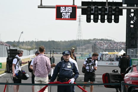 A security guard looks on at the starting grid as a sign shows a delayed start.