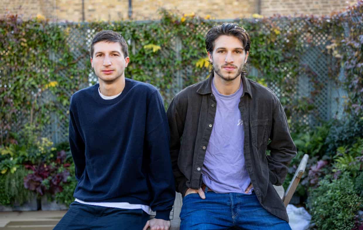 Sulaiman and Kasim Khan sit side by side outdoors in front of a leafy trellis