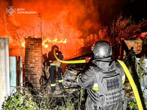 Firefighters carrying a hose approach a blaze