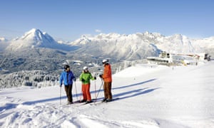 Three skiers about to set off in deep snow, mountains behind