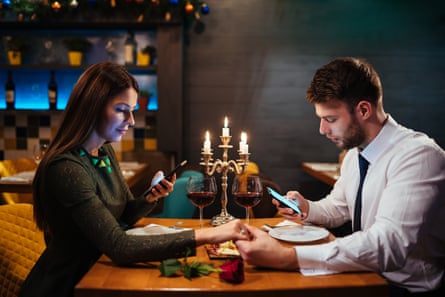 Couple holding hands at dinner and texting on the smart phone.