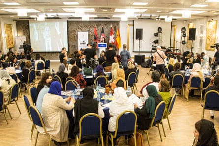 Groups of Afghan women sit around large tables in a conference hall