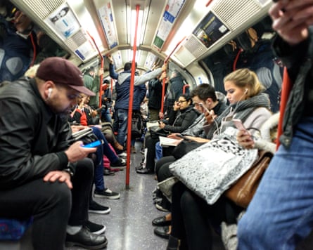 Passengers sit and stand inside a crowded London Underground carriage, many looking at their phones