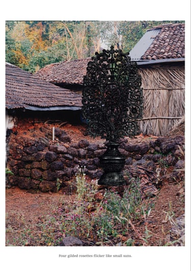 A blackened ornamental form appears before vernacular houses and laterite walls