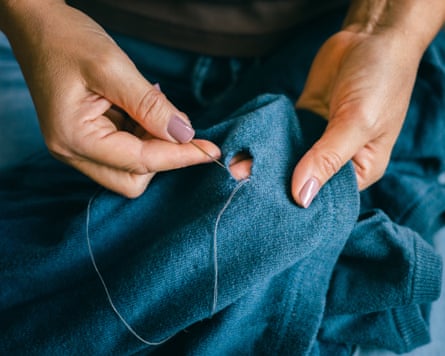 Closeup of hands stitching a hole in blue sweater with needle and thread during mending work