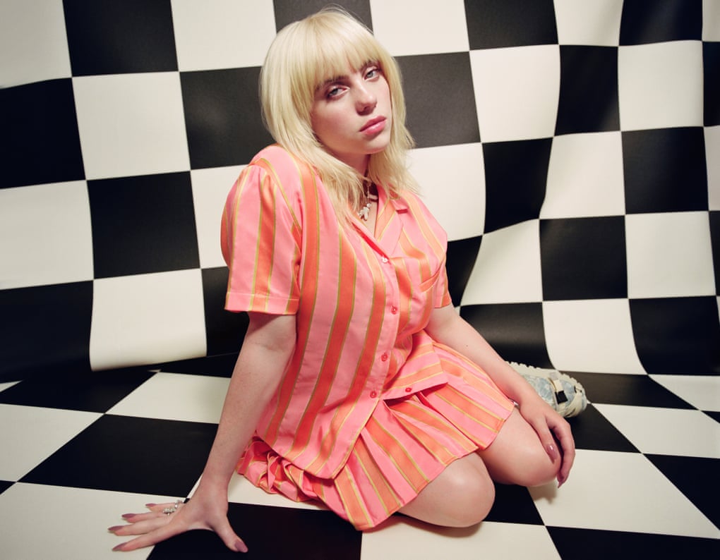 Billie Eilish in pink stripy outfit against black and white checked background