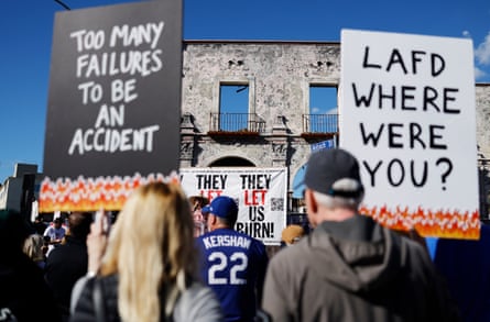 people hold signs that read ‘too many failures to be an accident’ and ‘LAFD where were you’