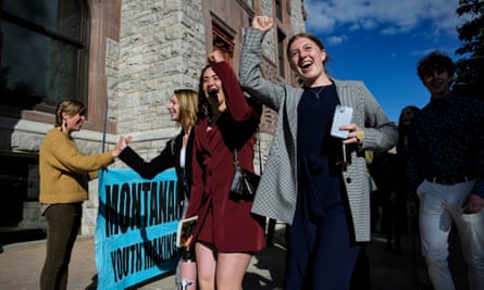 Young people dressed in skirt suits outside courthouse building pump fists and hold banners, smiling.