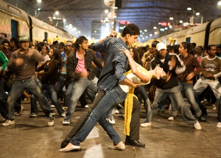 They dance in a railway station, with a busy crowd in the background