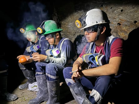 Three miners in helmets sit in a tunnel smoking