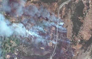Several plumes of smoke rise as a fire burns next to a road.