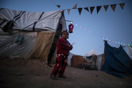 A displaced Palestinian child outside his familly's shelter as lanterns and Ramadan accessories decorate the tents in Deir Al Balah, southern Gaza Strip.