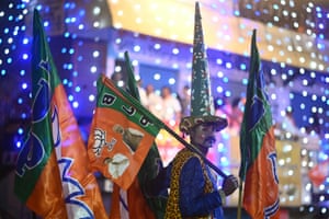 A Bharatiya Janata party supporter is wearing a pointy green hat with white flowers while holding a flag bearing an image of the Indian prime minister, Narendra Modi, in Bengaluru