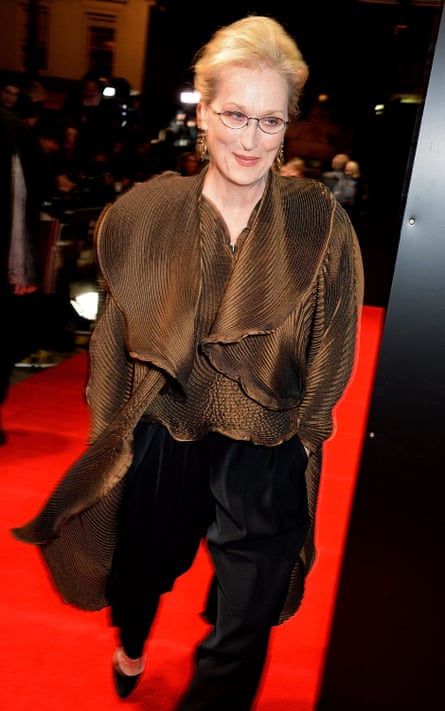 Meryl Streep walks a red carpet wearing a brown flowy pleated jacket