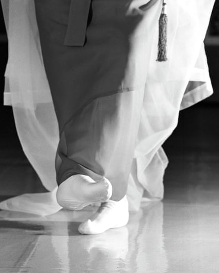 Close-up of feet in white socks beneath flowing traditional Korean robes, standing on a reflective floor