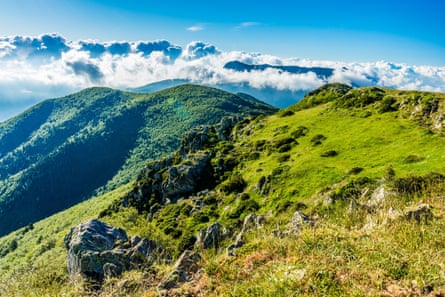 View fromt the top of a green peak overlooking other mountains on a sunny day