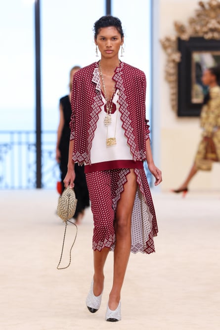 A model wearing a white tank top with a fine, loose, white-spotted burgundy jacket and skirt