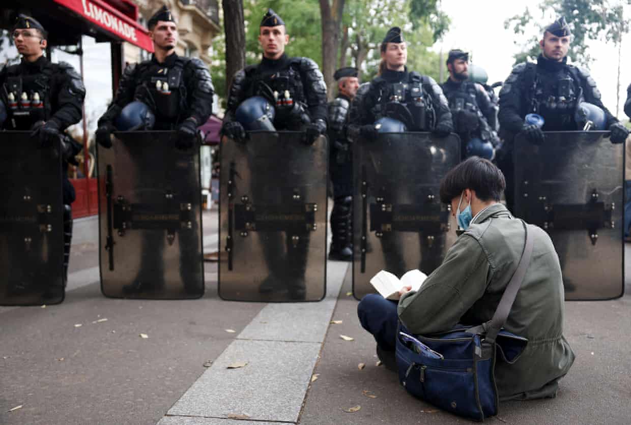 A demonstrator sits reading a book in front of gendarmerie officers holding riot shields