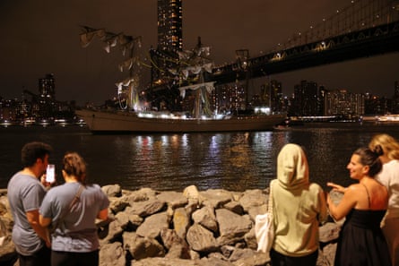 Multiple people stand in front of a rocky outcrop looking at a damaged vessel.