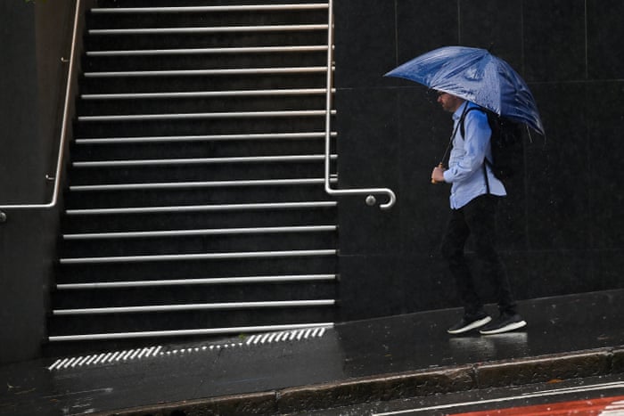 Members of the public take shelter from the rain under umbrellas in Sydney