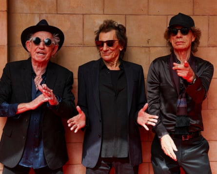 Keith Richards, Ronnie Wood and Mick Jagger standing against a wall