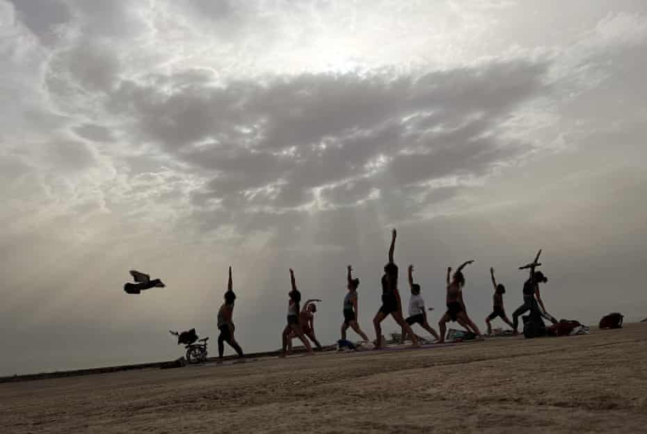 Men and women practice yoga on a breakwater by the Mediterranean sea in Barcelona, Spain