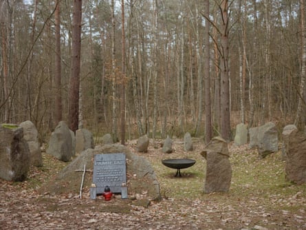 A memorial site including a fire bowl in the middle of a stone circle, and an engraved tablet mounted on a stone. The site is surrounded by trees
