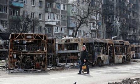 A local resident walks past burnt out buses in a street in Mariupol