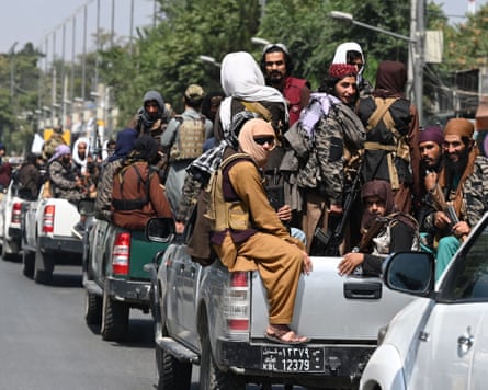 Afghan Taliban fighters ride in the back of pickup trucks in a convoy on a road in Kabul.