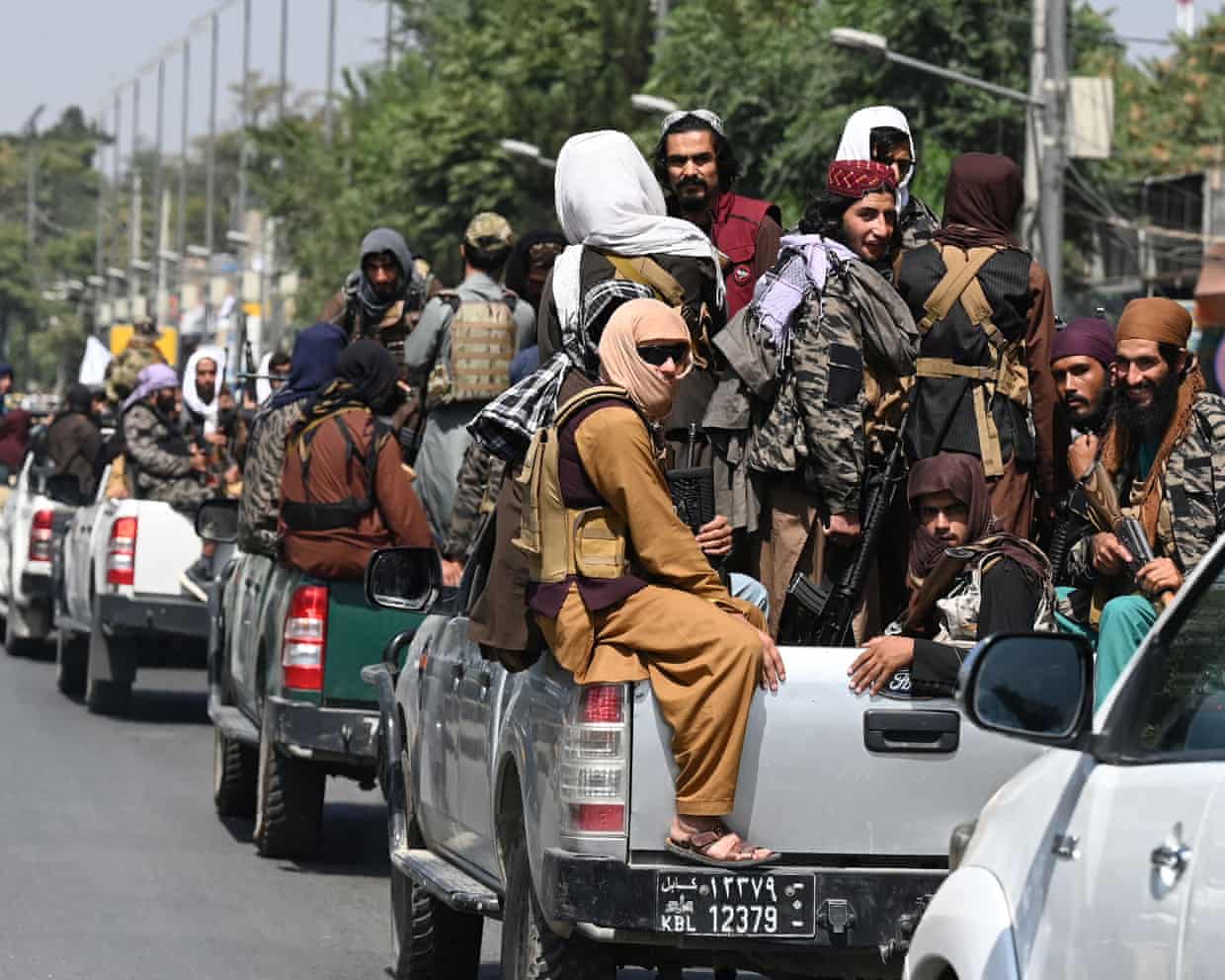 Afghan Taliban fighters ride in the back of pickup trucks in a convoy on a road in Kabul.