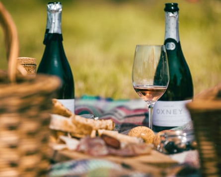Two bottles of sparkling English wine and a glass sit on a picnic blanket, surrounded by picnic food, at Oxney Organic Estate in Rye, Sussex, UK.