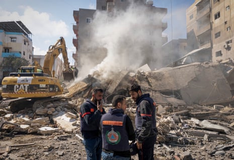 Rescue workers stand next to rubble and an excavator