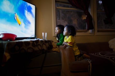 Two children watch TV on a large screen in a dark room.