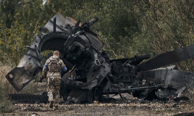 A Ukrainian soldier passes by a Russian tank damaged in a battle in the Kharkiv region.