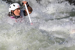 The head of a canoeist in a white helmet can be seen in raging water as she uses a paddle
