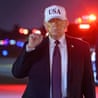 Donald Trump on tarmac with hat that says USA, raising power fist