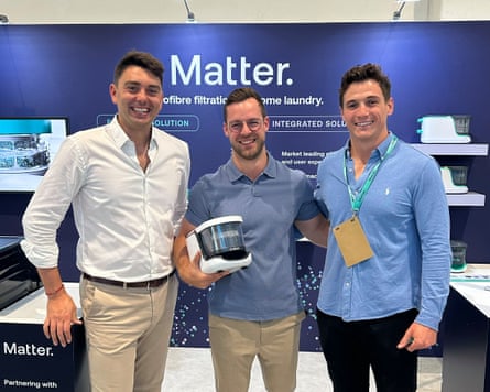 Three men stand in a line, with the man in the middle holding a small plastic device.