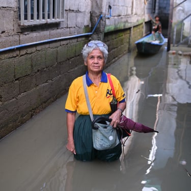 A woman stands thigh-deep in a flooded street in front of a small boat