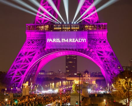 The Eiffel Tower is illuminated in vibrant pink and purple lights, featuring a massive projection that reads “PARIS, I’M READY.