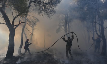 Smoke envelops firefighters who are using a hose to try to extinguish a wildfire