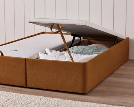 A tan and white storage bed. One side is open to reveal the storage of bedding inside