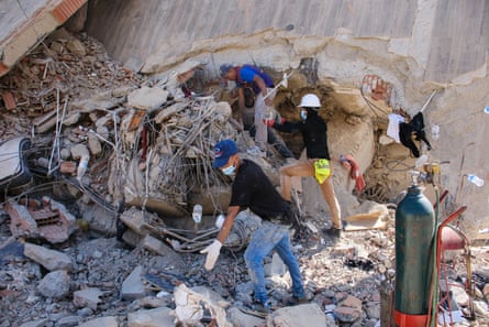 People in caps and gloves sift through a heap of rubble and chunks of concrete.
