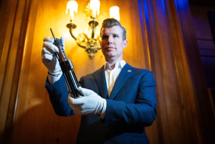 Man with white gloves holds lightsaber lit from behind