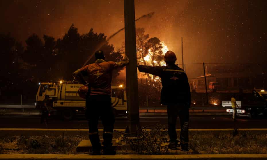 Volunteer firefighters watch as flames approach a highway in Afidnes, near Athens, Greece